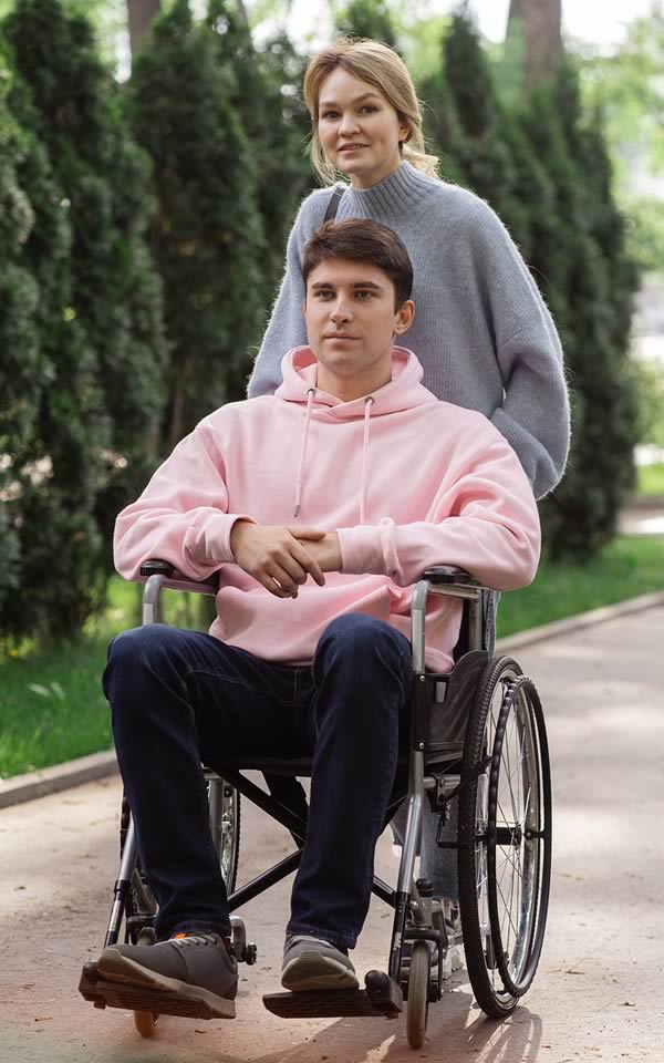 Young man in wheelchair with young woman pushing, in a park setting